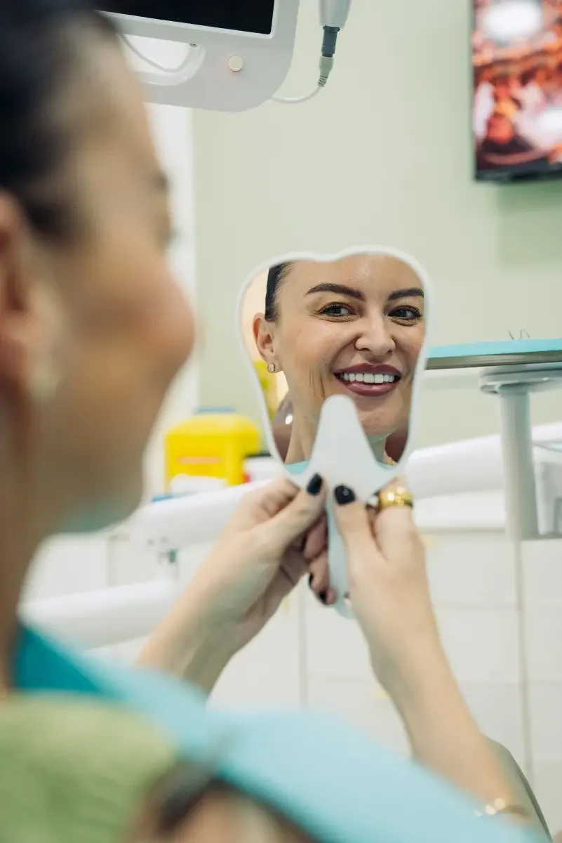 A patient looking at her smile in a hand mirror at Legacy Care